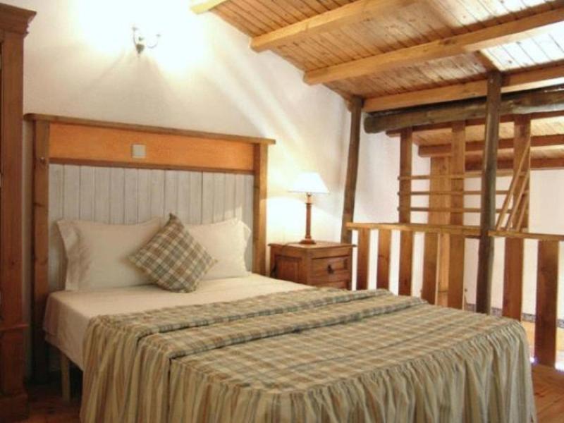 Gemütliches Schlafzimmer mit Holzbalken, Doppelbett, gestreiftem Bettüberwurf und Nachttischlampen.