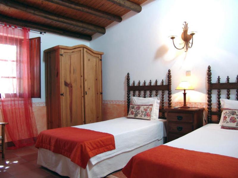 Schlafzimmer mit zwei Einzelbetten, Holzmöbeln und rotem Bett- und Fenstervorhang.