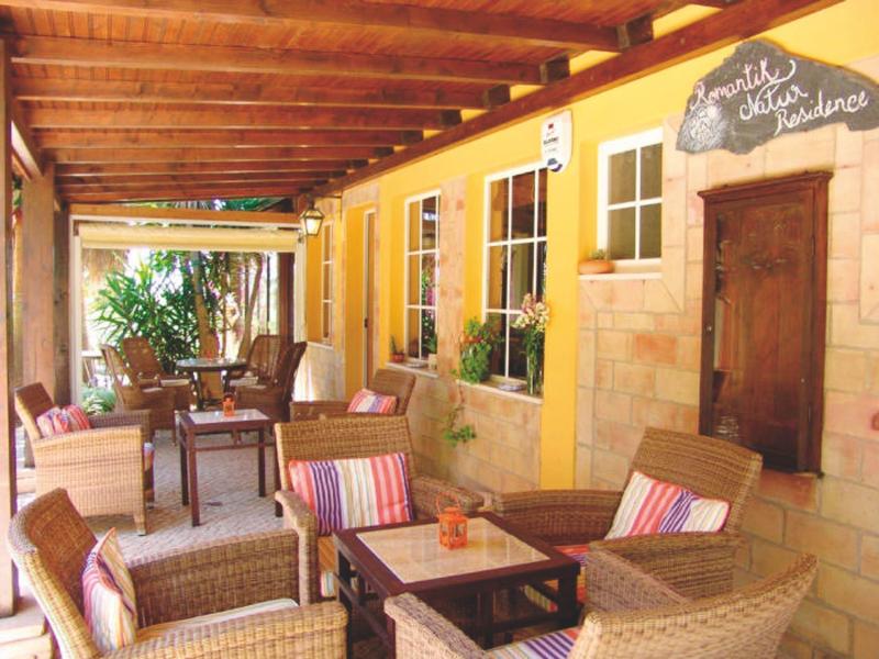 Gemütliche Terrasse mit Holzdach, Rattanmöbeln und bunten Kissen an gelber Hauswand.