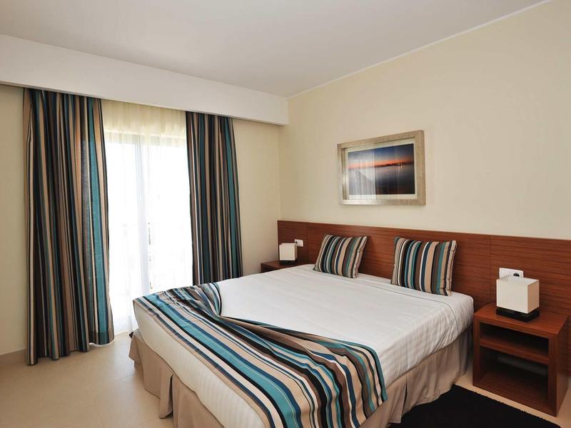 Ein schlichtes Schlafzimmer mit Doppelbett, gestreiften Betttextilien und einem Fenster mit Vorhängen.