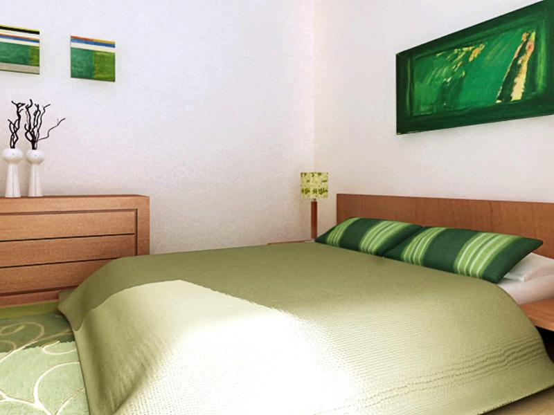 Schlafzimmer mit grünem Bett, Holzkommode, drei Vasen und drei grünen Wandbildern.