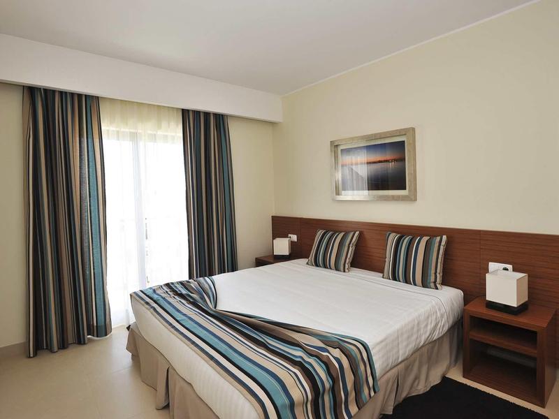 Modernes Schlafzimmer mit Doppelbett, Streifenbettwäsche in Blau- und Brauntönen, Vorhängen und Nachttisch.