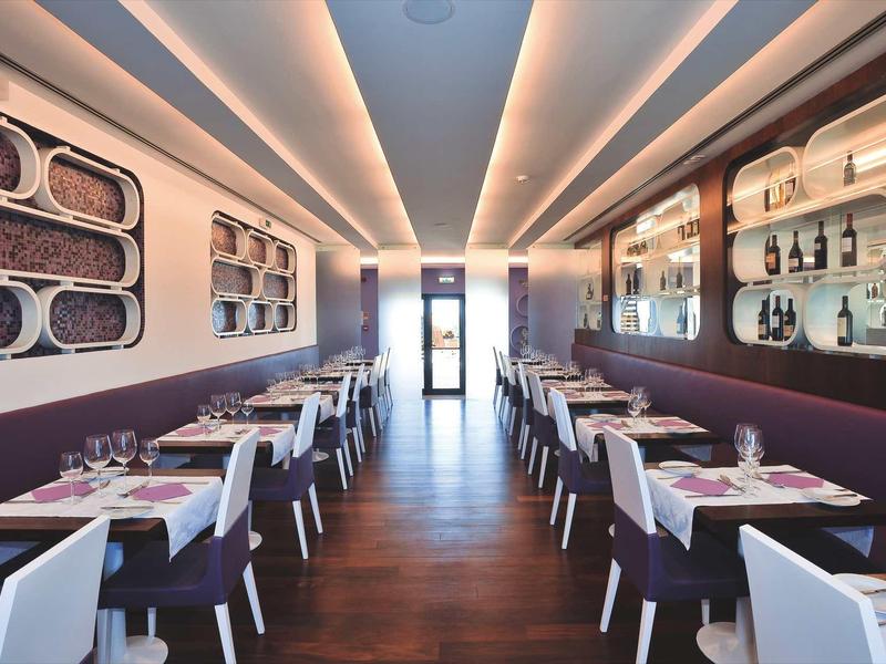 Modernes, elegantes Restaurant mit weißen Stühlen, dunklem Holzboden und warmem Deckenlicht.