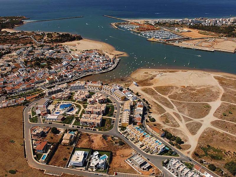Luftaufnahme einer Küstenstadt mit Wasserstraße, Sandflächen und Wohnvierteln mit Häusern und Straßen.