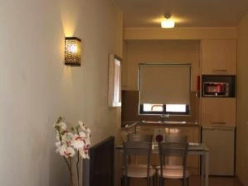 Kleiner Essbereich mit Glastisch, vier Stühlen, TV, Blumendeko und Wandlampe in schlichtem Raum.