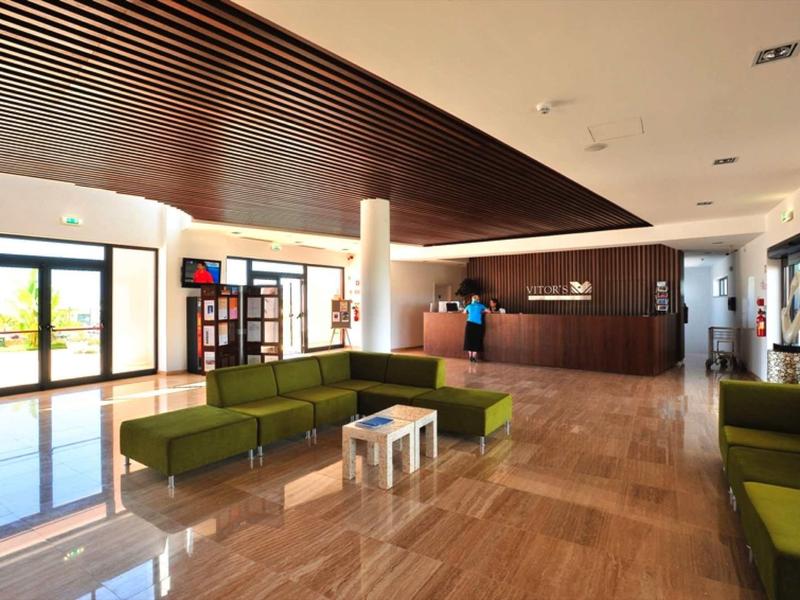 Große Hotellobby mit Glasfront, braunem Holz, grünen Sofas und hellbraunem Marmorboden.