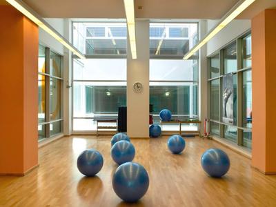 Palestra luminosa con pavimento in legno, grandi finestre e diverse palle da ginnastica blu.