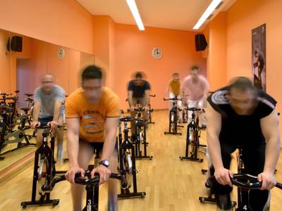 Persone si allenano su cyclette in una sala fitness luminosa.