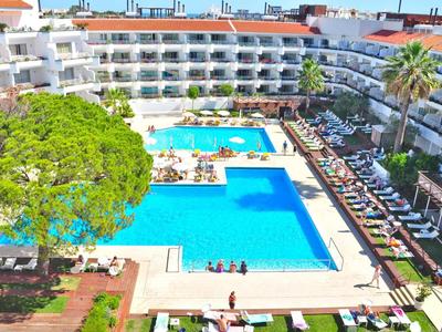 Großes blaues Schwimmbecken, umgeben von weißen Hotelgebäuden und grünen Bäumen.