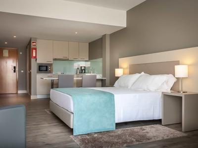 Modernes Hotelzimmer mit großem Bett, Küchenzeile, Holzfußboden und neutralen Wandfarben.