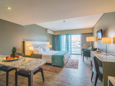 Hell eingerichtetes Hotelzimmer mit Doppelbett, Schreibtisch, Fernseher und Kleiderschrank, modern gestaltet.