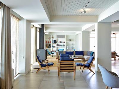 Helles Wohnzimmer mit blauer Sofa- und Stuhlgruppe, großem Fenster und Bücherregal an der Wand.