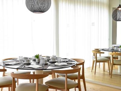 Moderner Essbereich mit rundem Esstisch, Holzstühlen, gedecktem Geschirr und großen Gardinen.
