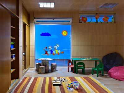 Kinderzimmer mit buntem Teppich, Spielzeug, grünem Tisch, Sitzsäcken und Wand mit Comic-Motiven.