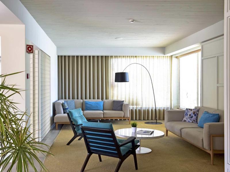 Modernes Wohnzimmer mit zwei Sofas, blauem Sessel, Stehlampe und großem Fenster im Hintergrund.