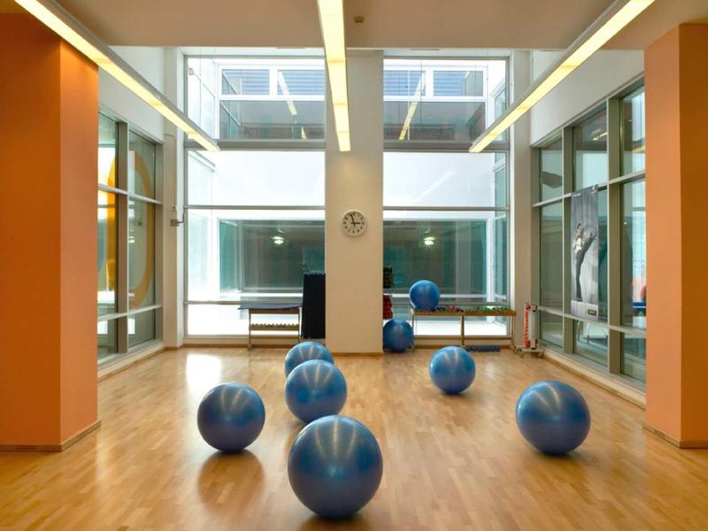 Innenraum mit Holzboden, Fensterfronten, orangen Säulen und mehreren blauen Gymnastikbällen.