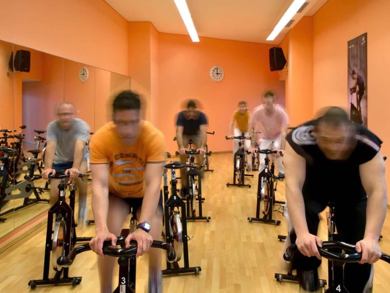 Mehrere Personen trainieren dynamisch auf stationären Fahrrädern in einem orangefarbenen Raum.