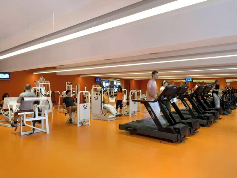 Moderne Fitnessstudio mit orangefarbenem Boden, Laufbändern und verschiedenen Trainingsgeräten.