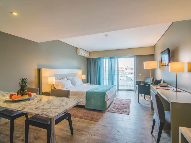 Hell eingerichtetes Hotelzimmer mit Doppelbett, Schreibtisch, Fernseher und Kleiderschrank, modern gestaltet.