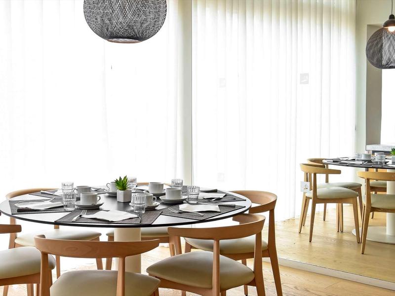 Moderner Essbereich mit rundem Esstisch, Holzstühlen, gedecktem Geschirr und großen Gardinen.