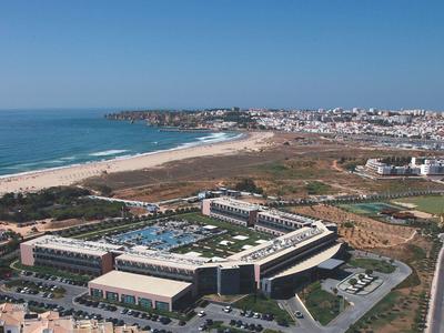 Große Hotelanlage mit Pool nahe sandigem Strand und städtischer Landschaft im Hintergrund.