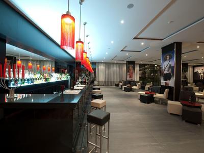 Moderner Barbereich mit roten Hängelampen, Barhockern und gemütlichen Sitzgruppen in hellem Raum.