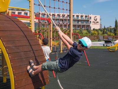Kind spielt auf Klettergerät mit Netz und Holzplatten auf Spielplatz bei klarem Himmel.