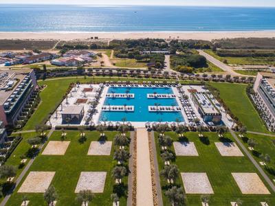 Luftaufnahme eines großen Schwimmbads mit angrenzenden Gebäuden und angrenzendem Ozean im Hintergrund.