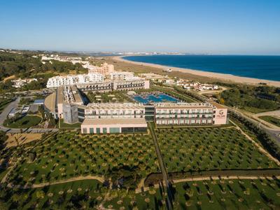 Großes Hotel mit Pool, Gartenanlagen und Strand am blauen Meer unter klarem Himmel.