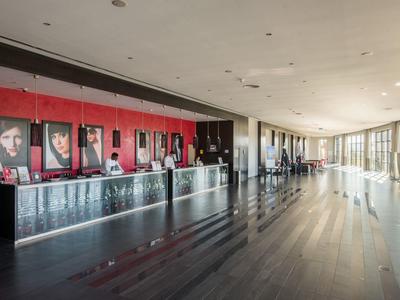 Weitläufiger Innenraum mit schwarzem Tresen, roten Wandbildern und großen Fenstern, hell beleuchtet.