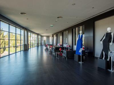 Moderner Ausstellungsraum mit großen Fenstern, dunklem Boden und Kleidern auf Schaufensterpuppen.