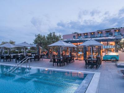 Abendstimmung am Pool mit beleuchteten Sitzbereichen und modernen Gebäuden im Hintergrund.