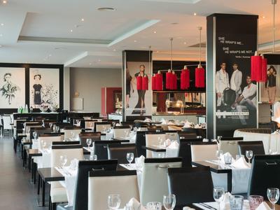 Modernes Restaurant mit weißen Tischtüchern, schwarzen Stühlen und roten Lampen, elegante Atmosphäre.