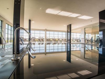 Modernes Hallenbad mit großem Fensterfront und klarer Wasseroberfläche, helle Deckenbeleuchtung.