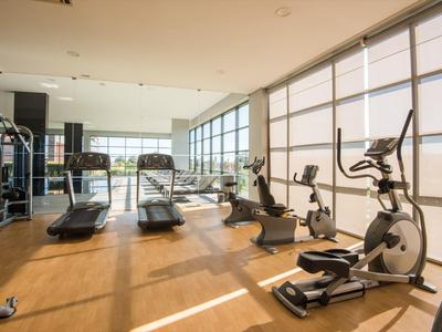 Moderner Fitnessraum mit Holzfußboden, großen Fenstern, Laufbändern und Trainingsgeräten.