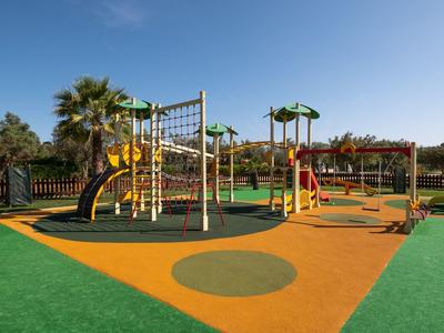 Bunter Spielplatz mit Klettergerüst, Rutschen und Schaukeln auf weichem Bodenbelag unter blauem Himmel.