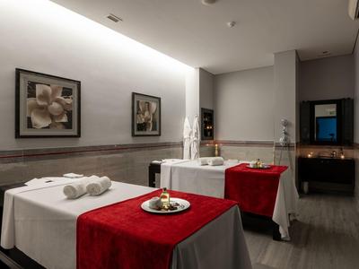 Ein ruhiger Wellnessraum mit zwei Massageliegen, rot-weiß dekoriert und gedämpftem Licht.