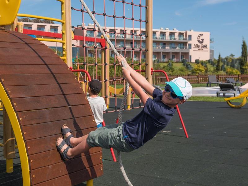 Kind spielt auf Klettergerät mit Netz und Holzplatten auf Spielplatz bei klarem Himmel.