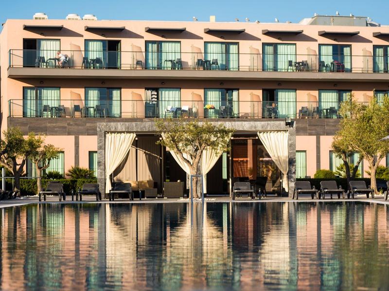 Ein großes Hotel mit mehreren Etagen und einem Pool im Vordergrund bei Sonnenuntergang.