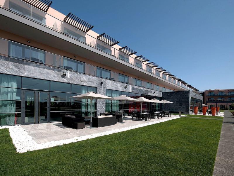 Modernes Gebäude mit Glasfront, Terrasse und grünem Rasen unter blauem Himmel.