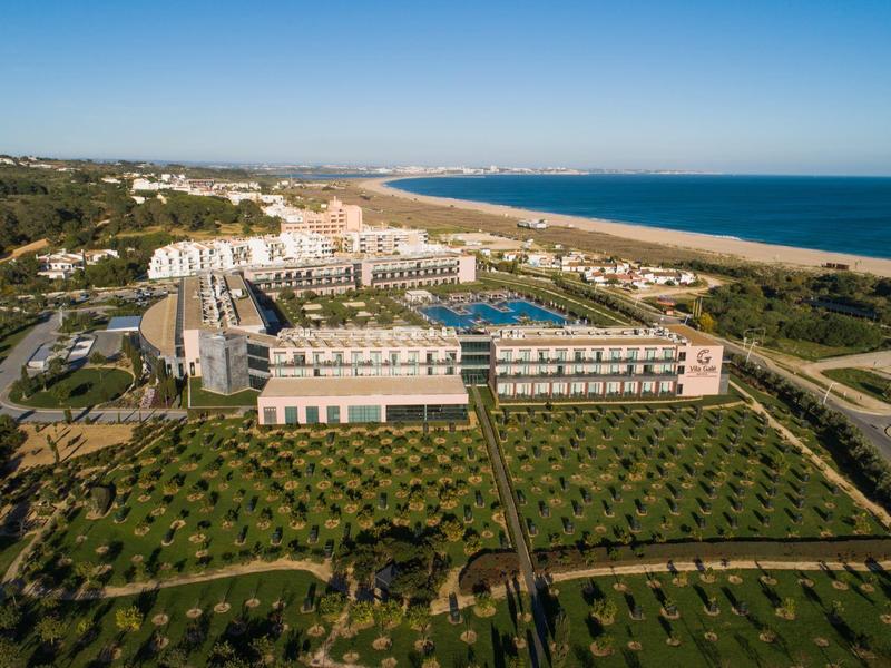Großes Hotel mit Pool, Gartenanlagen und Strand am blauen Meer unter klarem Himmel.