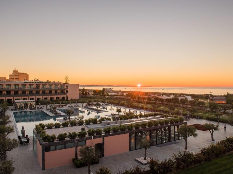 Großes Hotel mit Pool und Gastronomiebereich bei Sonnenuntergang am Meer in ruhiger Umgebung.