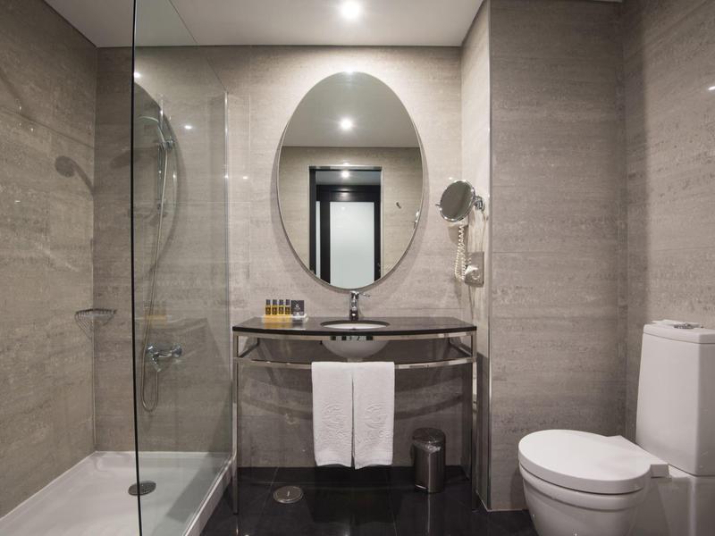 Modernes Badezimmer mit Glasdusche, ovalem Spiegel, Waschbecken und weißer Toilette.