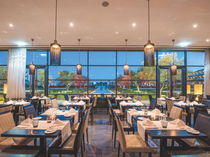 Modernes Restaurant mit großen Fensterfronten, Holztischen, braunen Stühlen und Blick auf Garten.