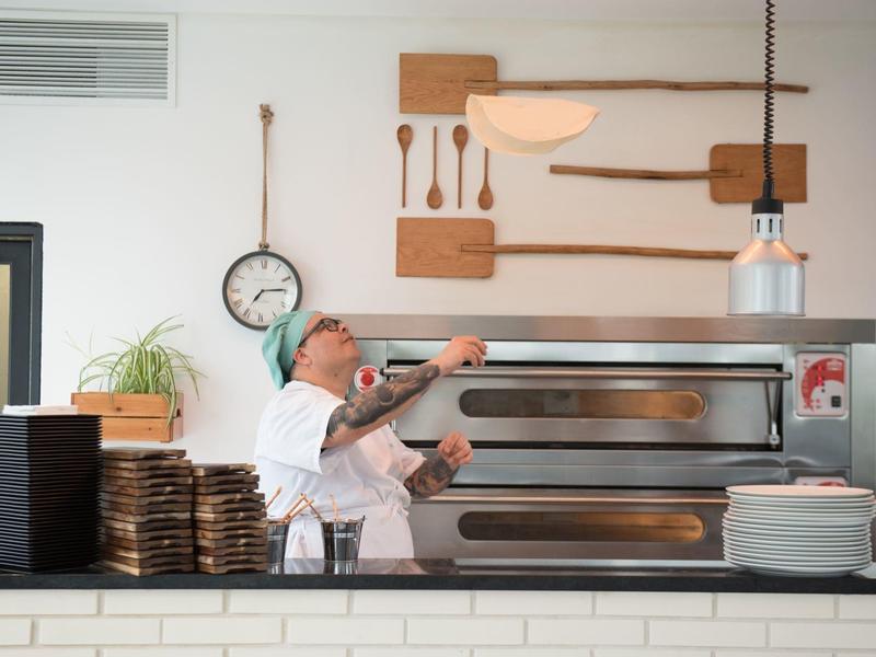 Pizzabäcker mit Bart wirft Pizzateig in einer modernen Küche über Lagertisch.