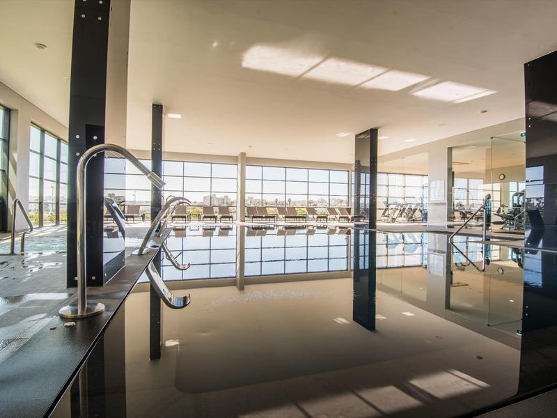 Modernes Hallenbad mit großem Fensterfront und klarer Wasseroberfläche, helle Deckenbeleuchtung.