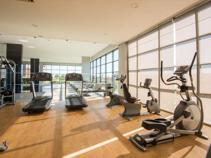 Moderner Fitnessraum mit Holzfußboden, großen Fenstern, Laufbändern und Trainingsgeräten.