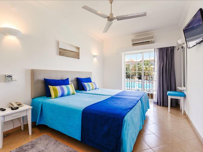 Helles Hotelzimmer mit Doppelbett, blauem Bettbezug und Balkon mit Blick ins Freie.