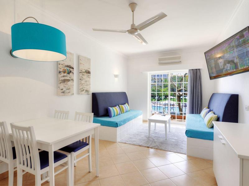 Helles Wohnzimmer mit blauem Sofa, Esstisch und Zugang zu Balkon mit Meerblick.