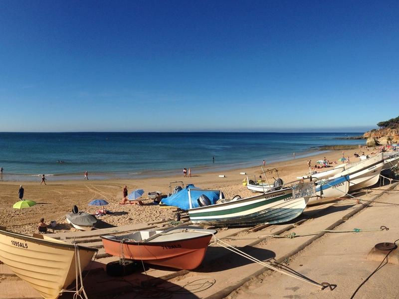 Strand mit mehreren Booten am Ufer und Menschen im Wasser bei klarem Himmel.
